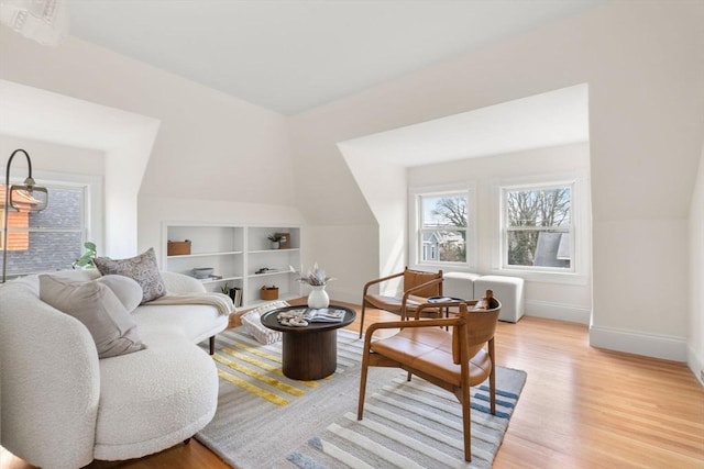 living area with built in shelves, baseboards, lofted ceiling, and light wood-style flooring