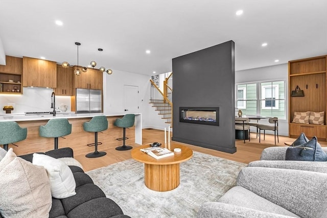 living area featuring a large fireplace, light wood-style flooring, stairs, and recessed lighting