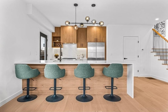 kitchen featuring light countertops, built in refrigerator, a kitchen bar, and brown cabinetry