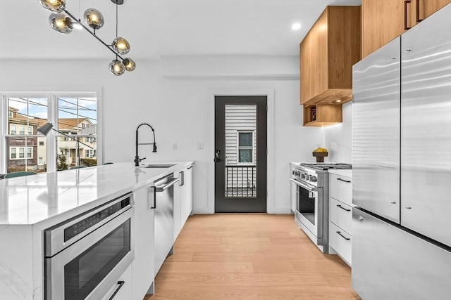 kitchen featuring a sink, modern cabinets, light wood-type flooring, a peninsula, and built in appliances