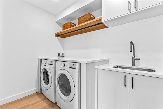 clothes washing area with cabinet space, light wood finished floors, baseboards, separate washer and dryer, and a sink