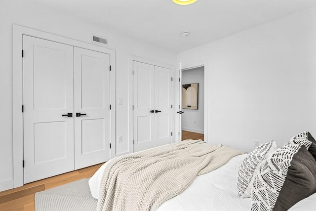 bedroom with visible vents, light wood finished floors, and two closets