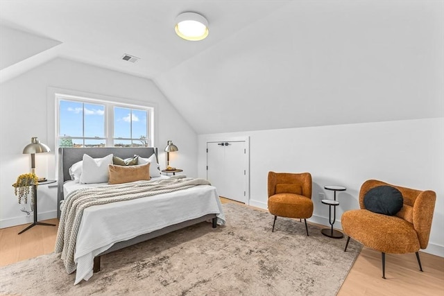 bedroom with lofted ceiling, wood finished floors, visible vents, and baseboards