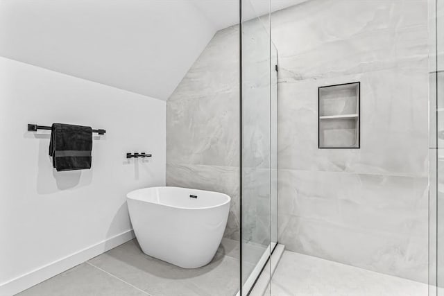 full bath with lofted ceiling, tile patterned flooring, baseboards, a freestanding bath, and a marble finish shower