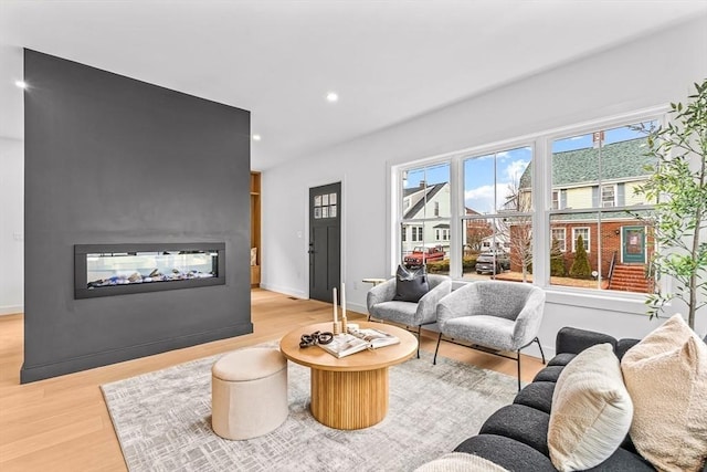 living room with baseboards, recessed lighting, a multi sided fireplace, and light wood-style floors