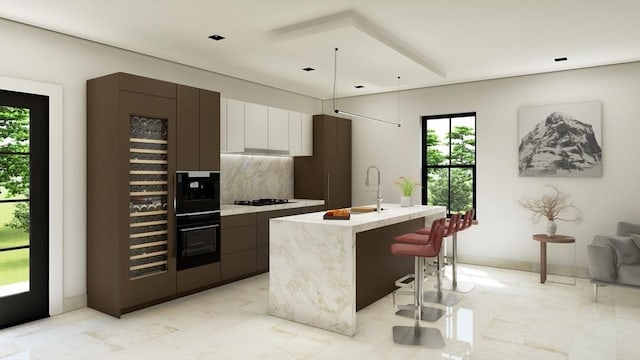 kitchen featuring black oven, tasteful backsplash, white cabinetry, a kitchen bar, and a kitchen island with sink