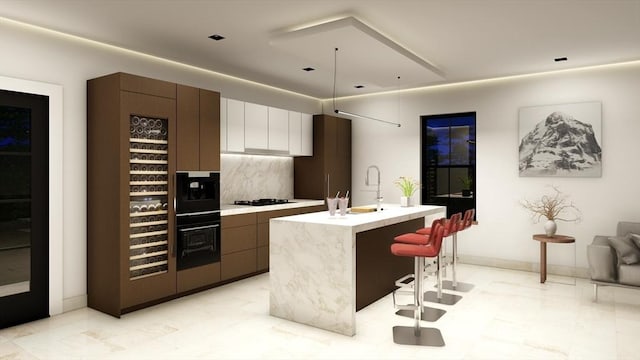 kitchen with an island with sink, oven, a kitchen breakfast bar, decorative backsplash, and gas stovetop