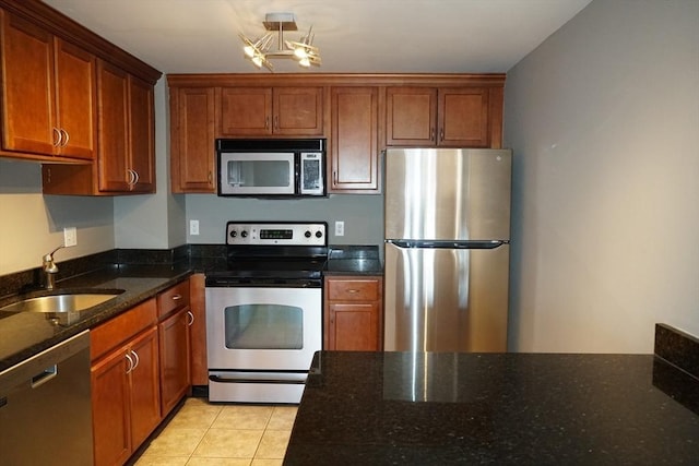 kitchen with sink, dark stone countertops, a chandelier, light tile patterned floors, and appliances with stainless steel finishes