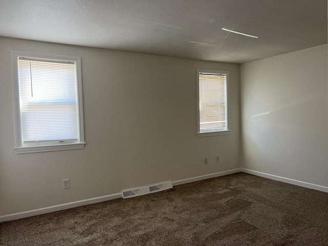 spare room featuring baseboards, visible vents, and dark colored carpet