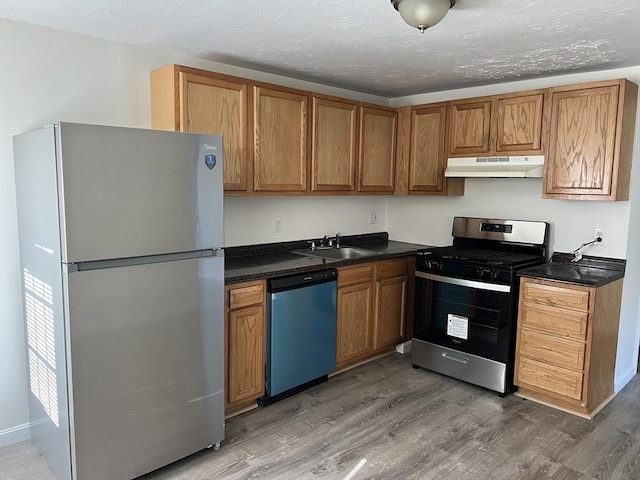 kitchen with stainless steel appliances, dark countertops, under cabinet range hood, and wood finished floors