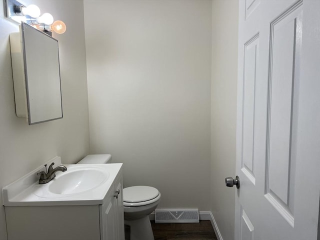 half bath with visible vents, toilet, vanity, wood finished floors, and baseboards