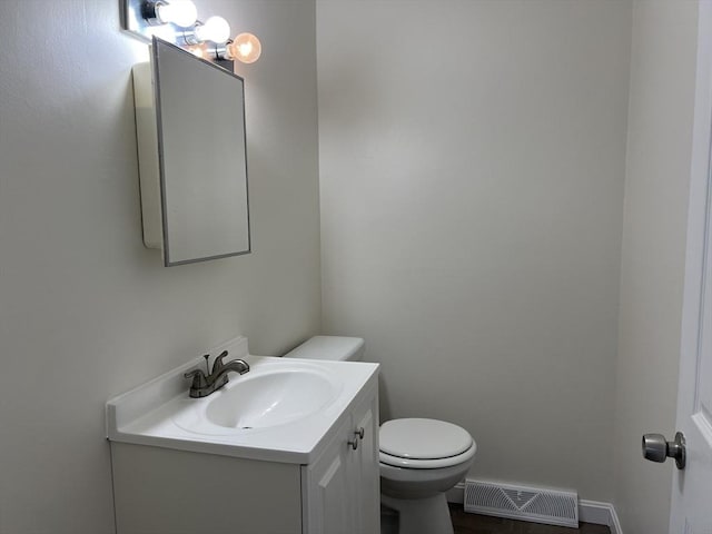 half bathroom with toilet, baseboards, visible vents, and vanity