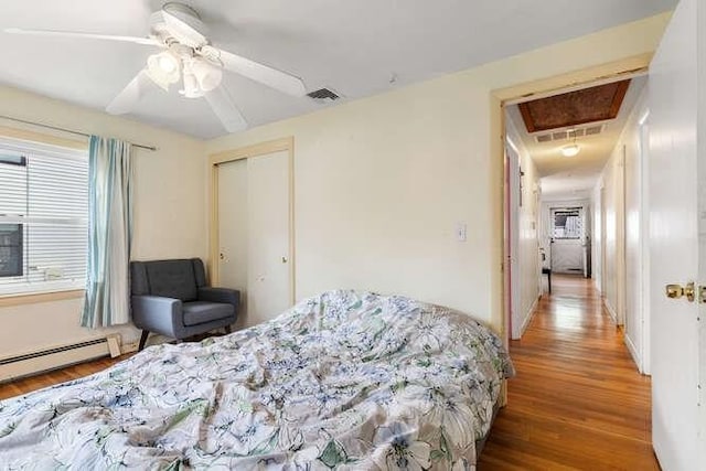 bedroom with attic access, visible vents, baseboard heating, wood finished floors, and a closet