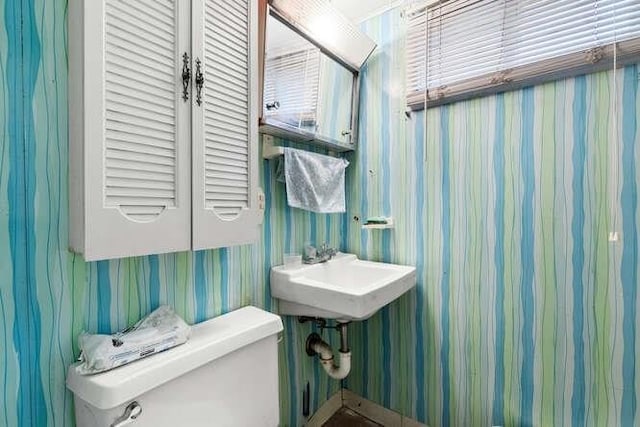 half bathroom with a sink, toilet, and wallpapered walls