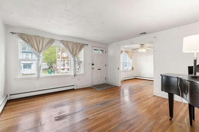 unfurnished living room featuring a baseboard radiator, ceiling fan, wood finished floors, and a wealth of natural light