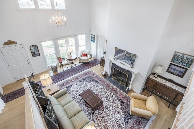 living area featuring a high ceiling, a chandelier, wood finished floors, a high end fireplace, and baseboards