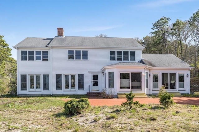 back of property featuring entry steps, a chimney, and a shingled roof