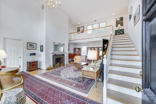 living room featuring a towering ceiling, healthy amount of natural light, stairway, a fireplace, and a chandelier