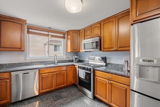 kitchen with sink, hanging light fixtures, dark stone counters, and appliances with stainless steel finishes