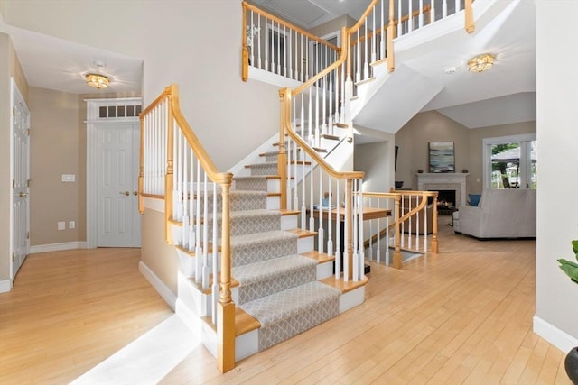 stairway with a towering ceiling, baseboards, hardwood / wood-style flooring, and a fireplace