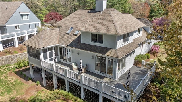 rear view of house with a sunroom, a shingled roof, a chimney, and a deck