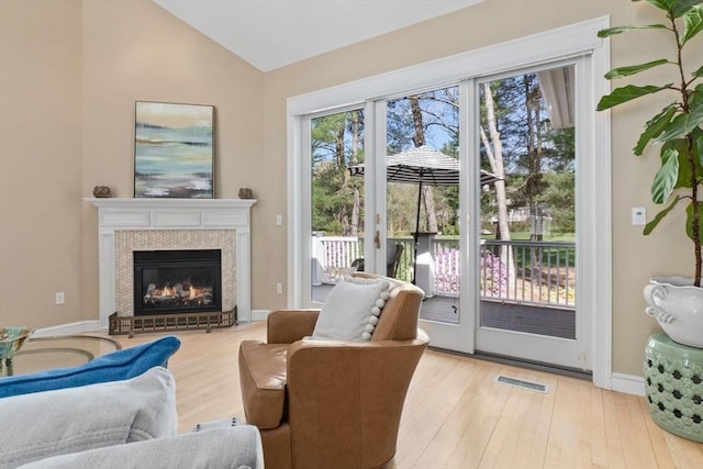 interior space with visible vents, a glass covered fireplace, wood finished floors, and vaulted ceiling