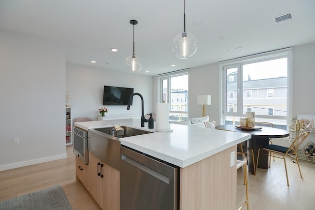 457 W Broadway Unit 209, Boston, MA 02127 - kitchen featuring stainless steel dishwasher, light wood finished floors, light brown cabinetry, an island with sink, and open floor plan