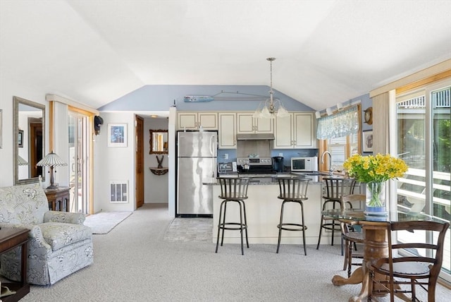 kitchen featuring dark countertops, lofted ceiling, a peninsula, stainless steel appliances, and cream cabinetry