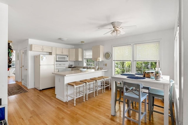 kitchen featuring white appliances, ceiling fan, a peninsula, light countertops, and light wood-type flooring