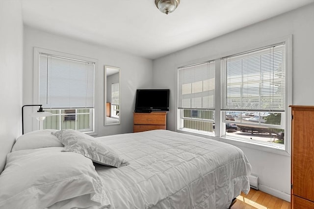 bedroom with a baseboard radiator, baseboards, and wood finished floors