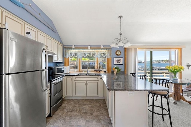 kitchen with a peninsula, cream cabinets, vaulted ceiling, stainless steel appliances, and a sink