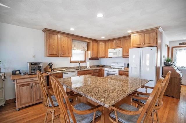 kitchen featuring white appliances, light stone counters, light hardwood / wood-style floors, and a breakfast bar area