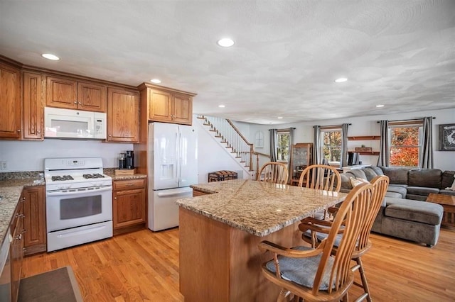 kitchen with light hardwood / wood-style floors, a breakfast bar area, a kitchen island, light stone countertops, and white appliances