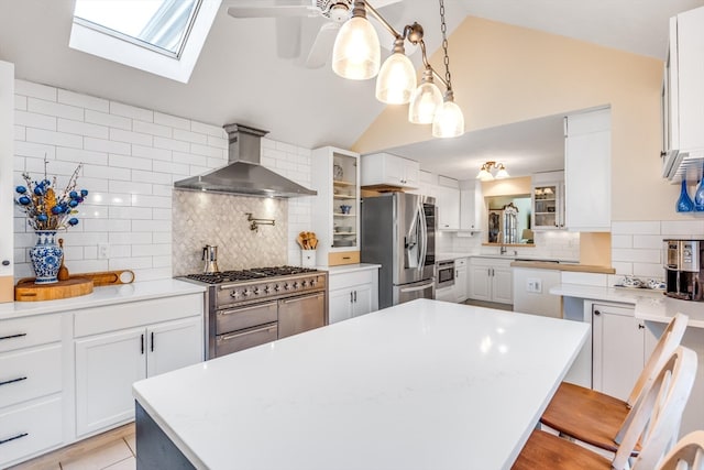 kitchen featuring wall chimney exhaust hood, a center island, appliances with stainless steel finishes, a kitchen breakfast bar, and white cabinets