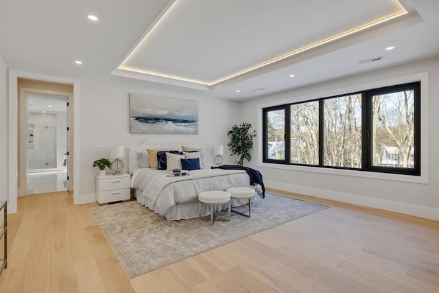 bedroom featuring connected bathroom, a tray ceiling, and light wood-type flooring