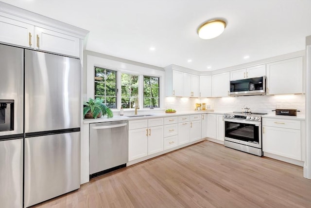 27 Lantern Ln, Arlington, MA 02474 - kitchen with appliances with stainless steel finishes, light countertops, decorative backsplash, white cabinetry, and light wood-type flooring