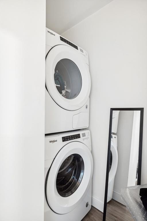 laundry room featuring laundry area, wood finished floors, baseboards, and stacked washer and dryer