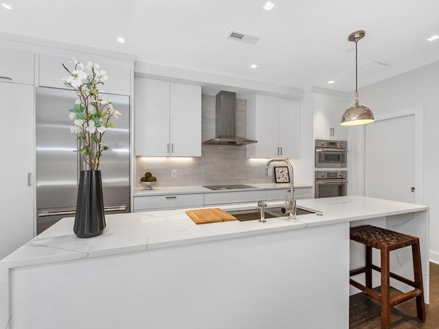 kitchen featuring pendant lighting, appliances with stainless steel finishes, wall chimney exhaust hood, white cabinets, and decorative backsplash