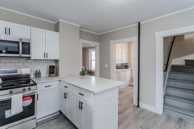 kitchen with kitchen peninsula, appliances with stainless steel finishes, light stone counters, crown molding, and white cabinets