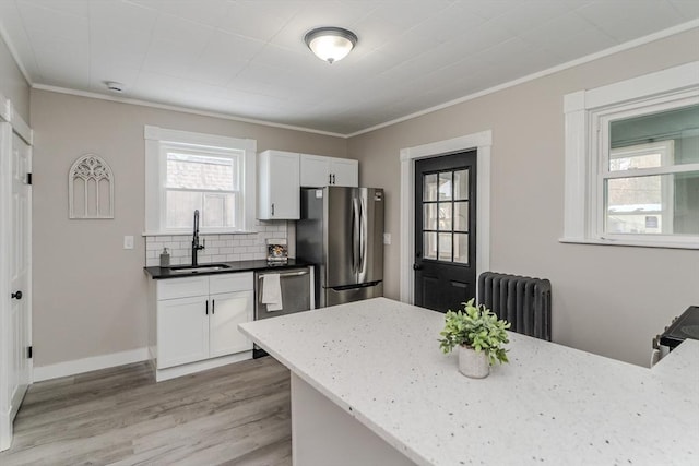 kitchen with radiator, white cabinets, sink, light wood-type flooring, and stainless steel appliances