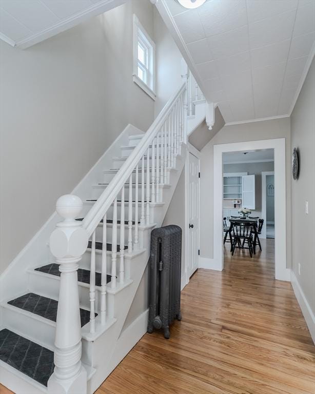 stairs with wood-type flooring and ornamental molding