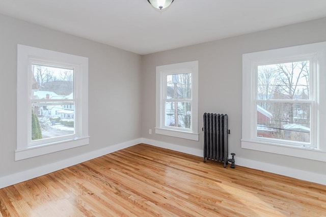 spare room with radiator heating unit, light hardwood / wood-style floors, and a healthy amount of sunlight