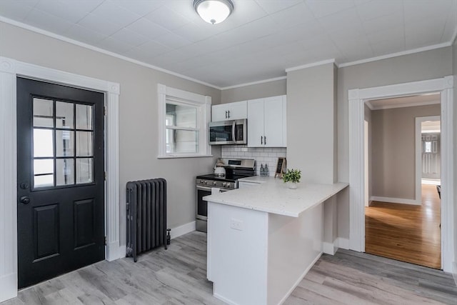 kitchen with radiator heating unit, backsplash, appliances with stainless steel finishes, white cabinets, and light wood-type flooring