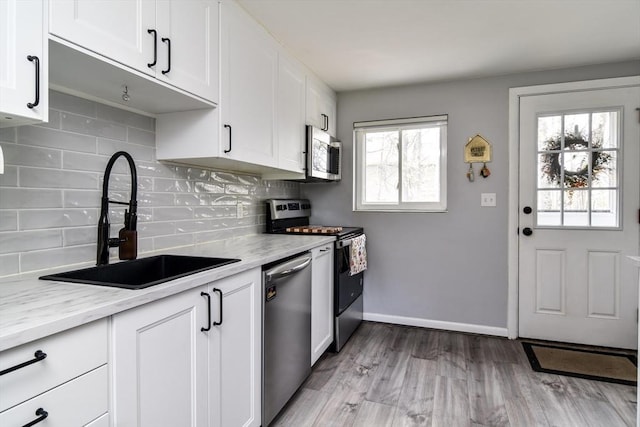kitchen featuring white cabinets, appliances with stainless steel finishes, a sink, and tasteful backsplash