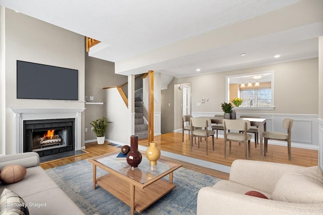 living area with a fireplace with flush hearth, a wainscoted wall, stairs, wood finished floors, and a decorative wall