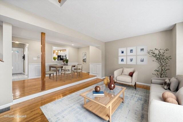 living area featuring visible vents, wood finished floors, wainscoting, and a decorative wall