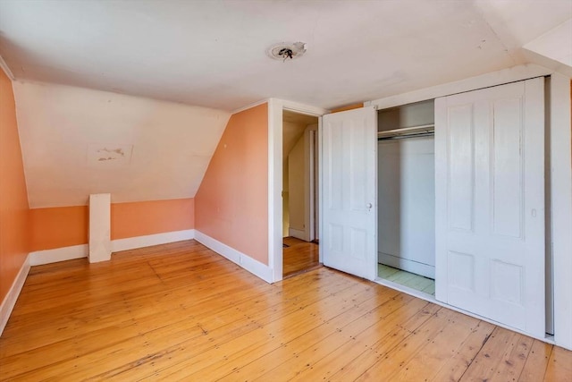 unfurnished bedroom with vaulted ceiling, light wood-type flooring, and a closet