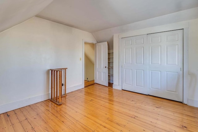 unfurnished bedroom featuring lofted ceiling, a closet, and light wood-type flooring