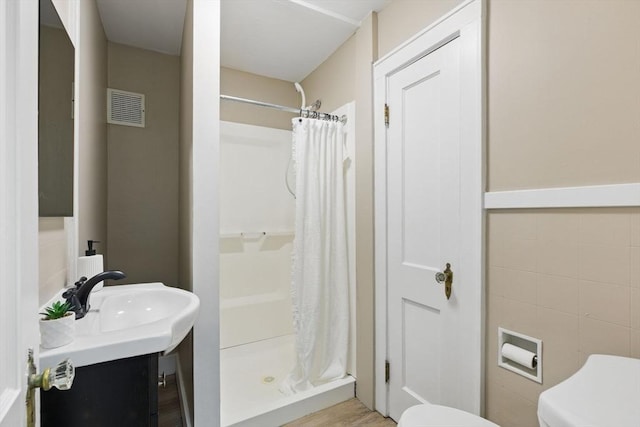 bathroom featuring toilet, vanity, visible vents, tile walls, and a stall shower