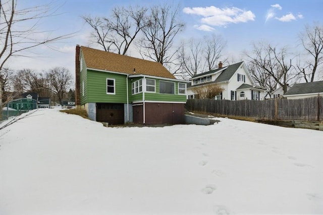 snow covered back of property featuring a sunroom, fence, a chimney, and an attached garage